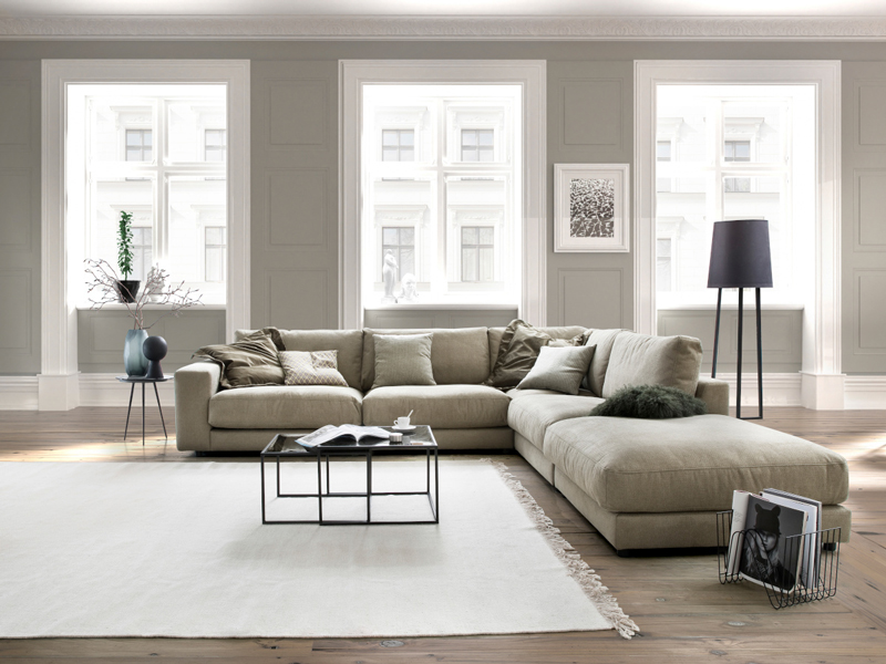 Großes Sofa in L Form um einen weißen Teppich mit drei große Fenster dahinter